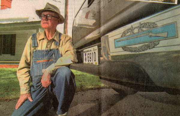 John Cullars McCrimmon, of Lincolnton, Ga., crouches by his truck, which bears a Purple Heart license tag and a sticker of the Combat Infantryman Third Award for serving in three wars in the U.S. Army, including the Korean War.