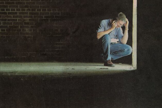 A man in a darkened warehouse kneeling and talking on a cell phone at Fort Gordon, Georgia.